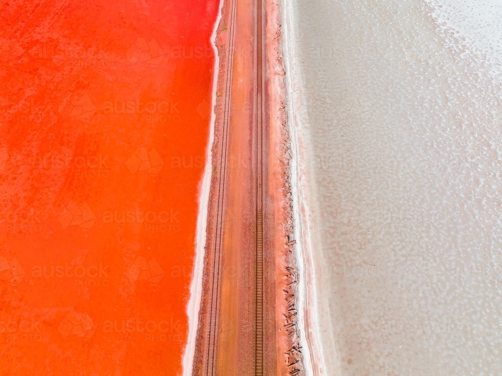 Aerial view of a railway line running across a salt lake with one side vivid red in colour - Australian Stock Image