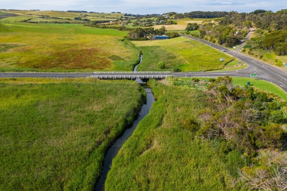 Aerial view of a river flowing under a road bridge through a green valley - Australian Stock Image