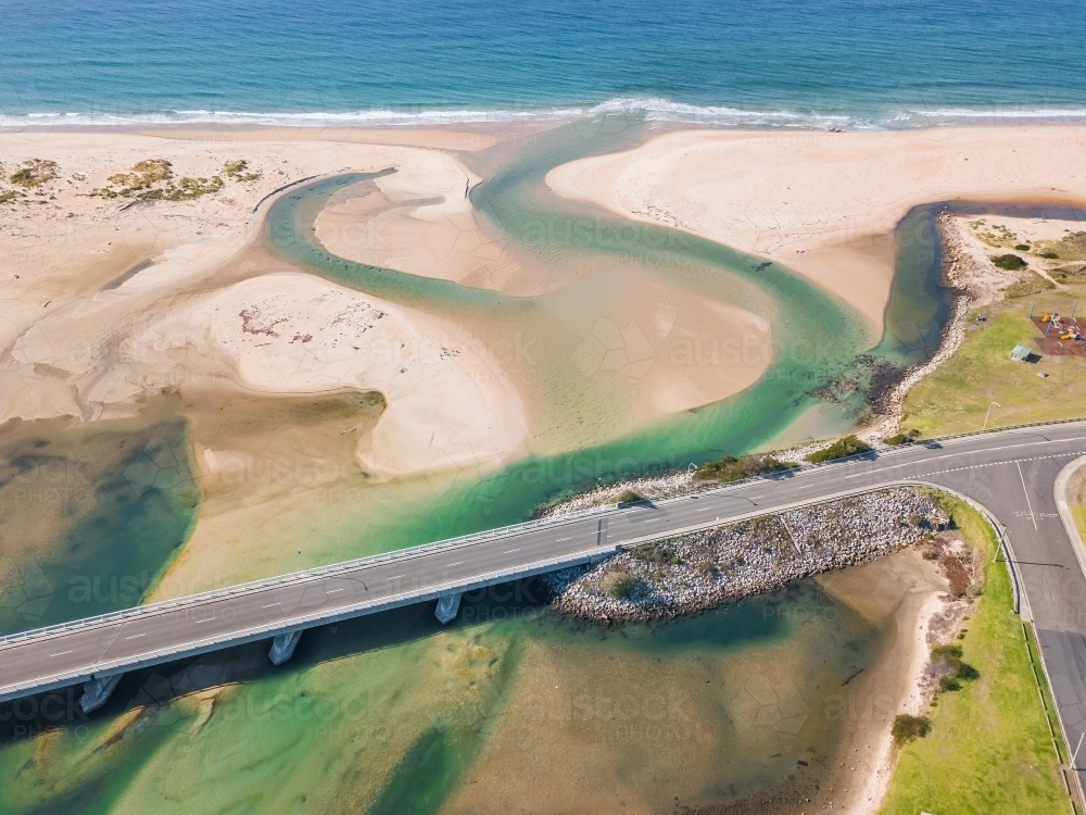 Aerial view of a river flowing under a road bridges and winding out to sea. - Australian Stock Image