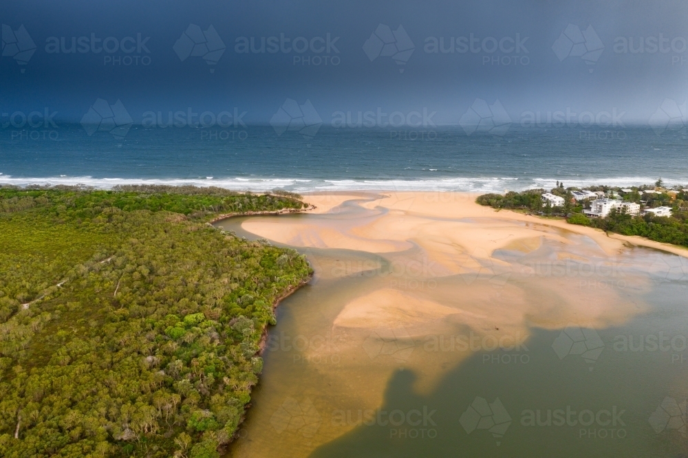 Aerial view of a river winding its way around sand bars and out to sea under a dark sky - Australian Stock Image