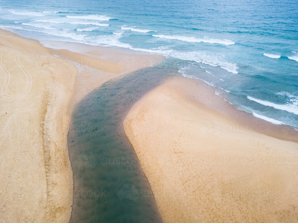 Aerial view of a river winding through a beach and out to sea - Australian Stock Image