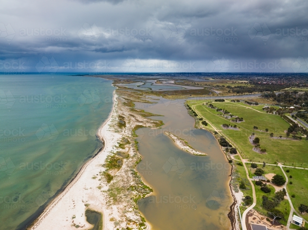 Aerial view of a sand bar running along a coastline under dark rain clouds - Australian Stock Image