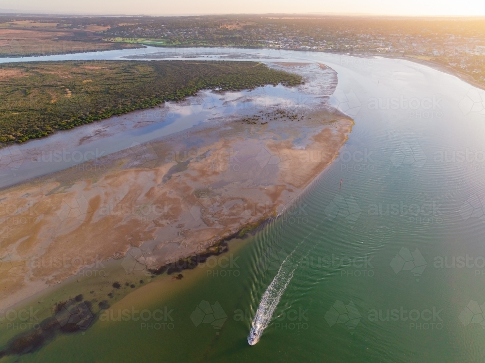 Aerial view of a small boat creating a wake in a wide coastal river - Australian Stock Image