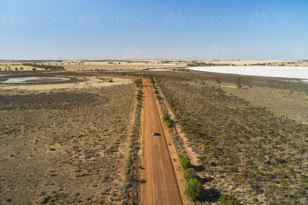 Aerial view of a small silver SUV driving on dirt roads through dry salt lakes in rural WA - Australian Stock Image