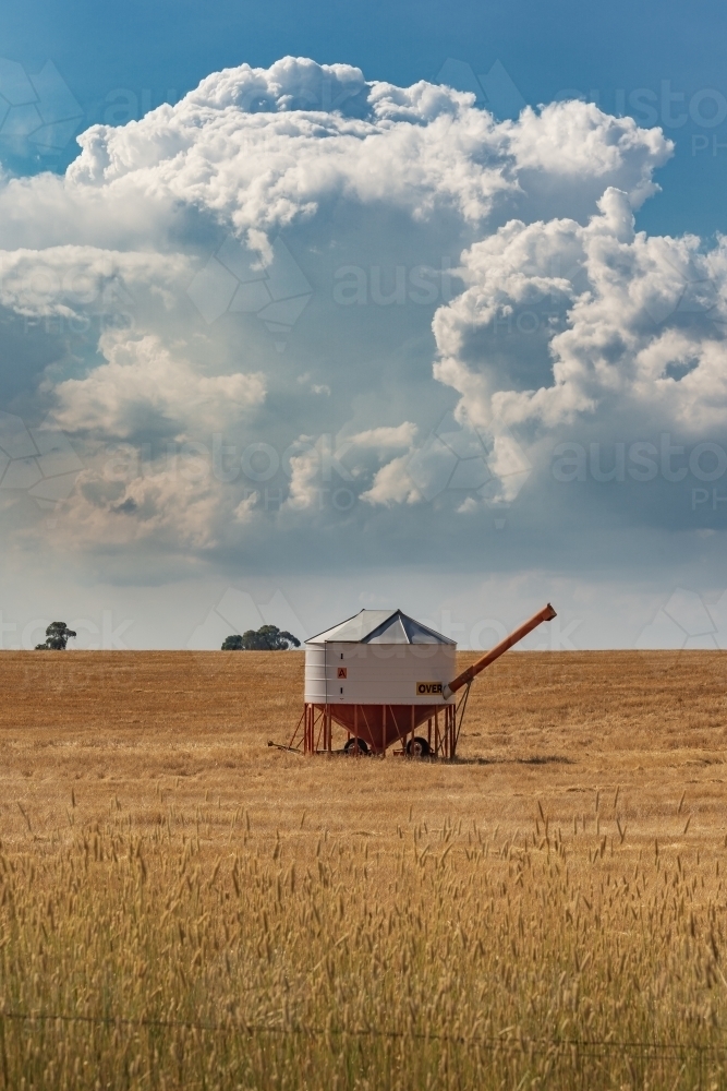 Aerial view of a solitary field bin sitting in a large barren paddock under a large storm cloud - Australian Stock Image