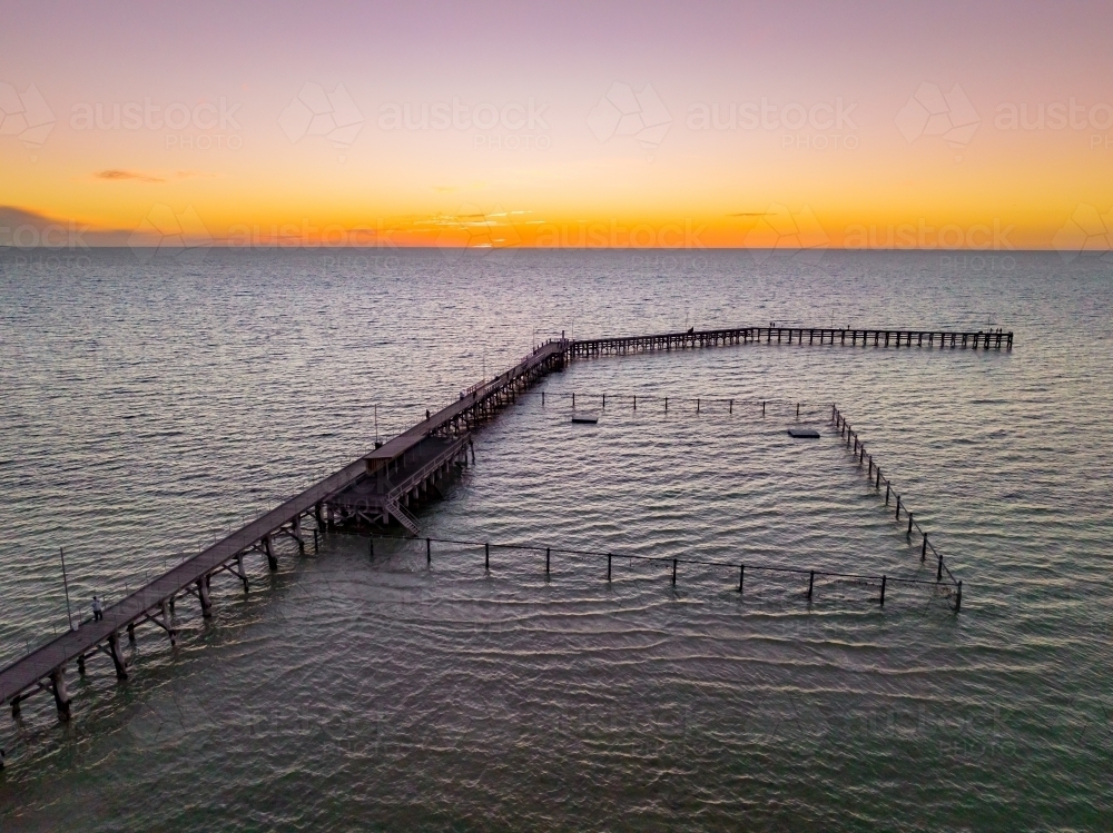 Aerial view of a sunset glow over a coastal jetty with a swimming enclosure - Australian Stock Image