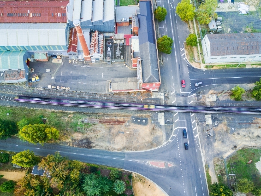 Aerial view of a train racing through a crossing beside a factory - Australian Stock Image