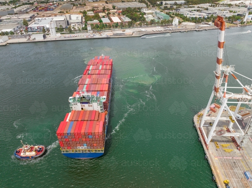 Aerial view of a tugboat moving a large cargo ship at a port - Australian Stock Image