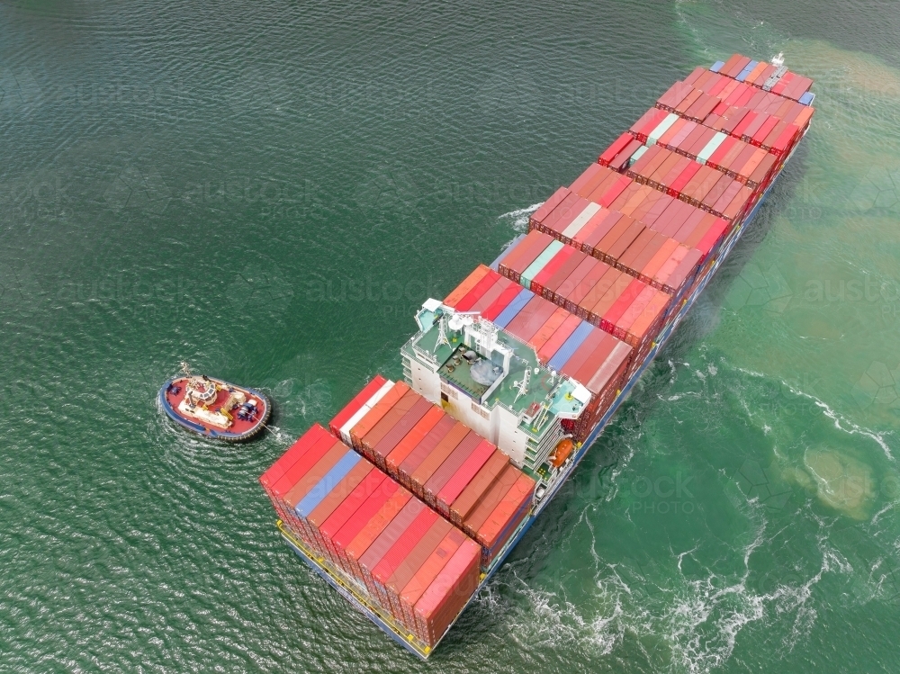 Aerial view of a tugboat moving a large cargo ship - Australian Stock Image