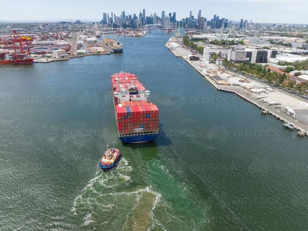 Aerial view of a tugboat moving a large cargo ship up a river - Australian Stock Image