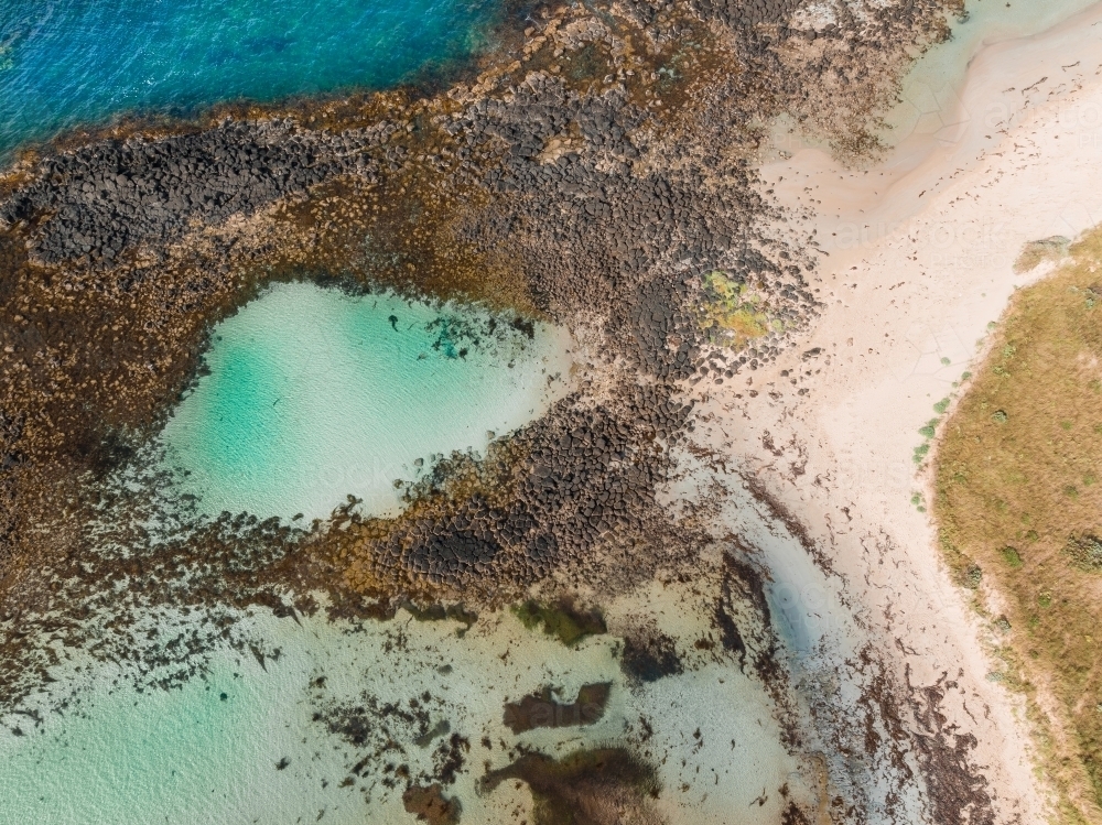 Aerial view of a turquoise blue rockpool alongside a sandy beach - Australian Stock Image