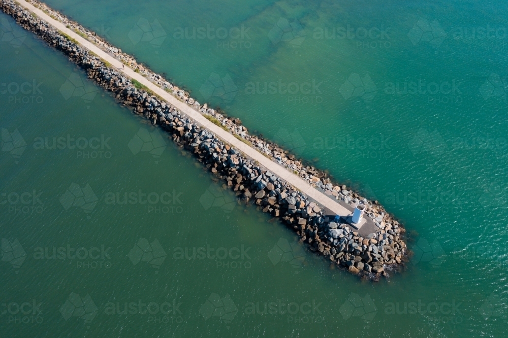 Aerial view of a warning beacon on the end of a rocky breakwater surrounded by sea - Australian Stock Image