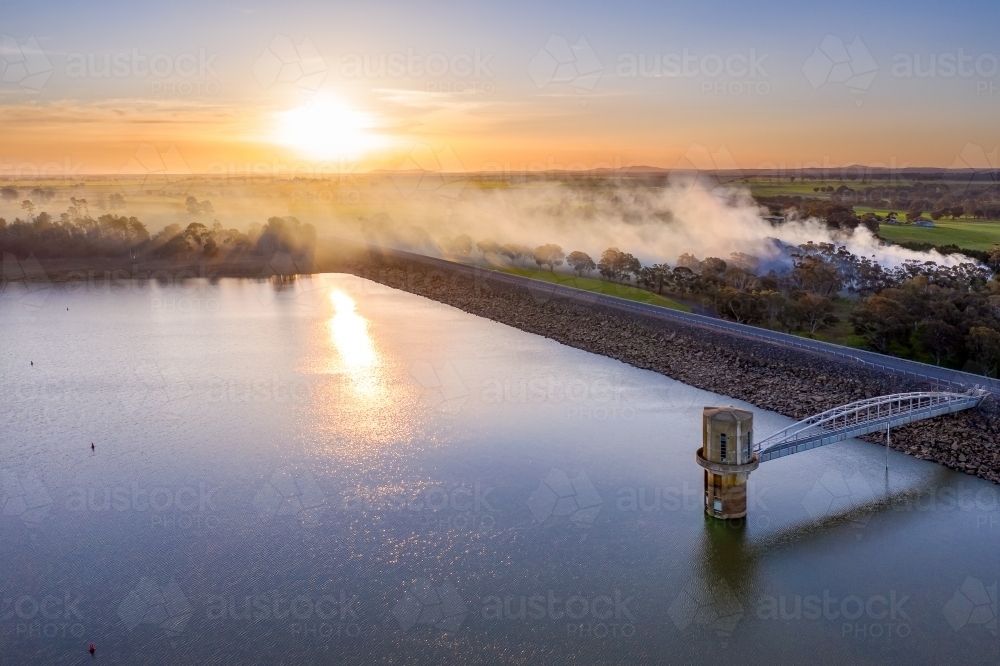 Aerial view of a water tower in a reservoir at sunset with smoke drifting across. - Australian Stock Image