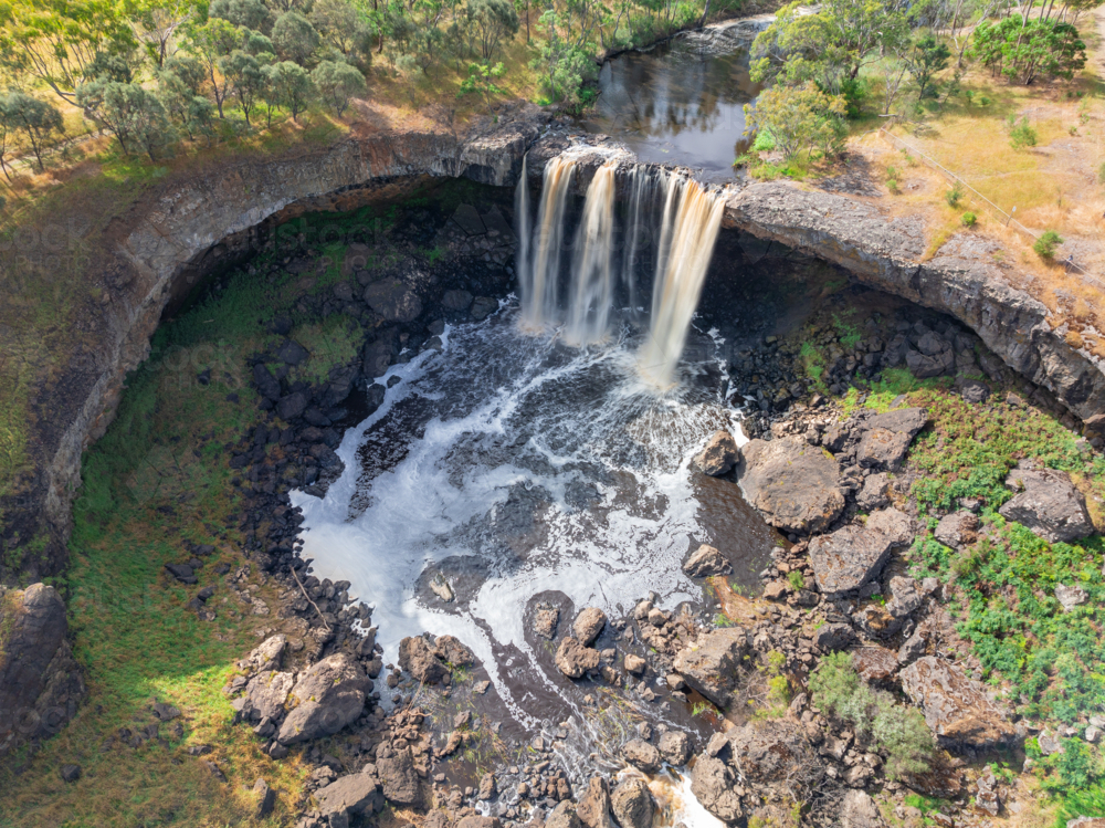 Aerial view of a waterfall cascading over the edge of a rock ledge into a pool below - Australian Stock Image