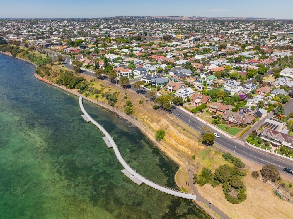 Aerial view of a winding boardwalk alongside coastal parkland and bay side waterfront property - Australian Stock Image