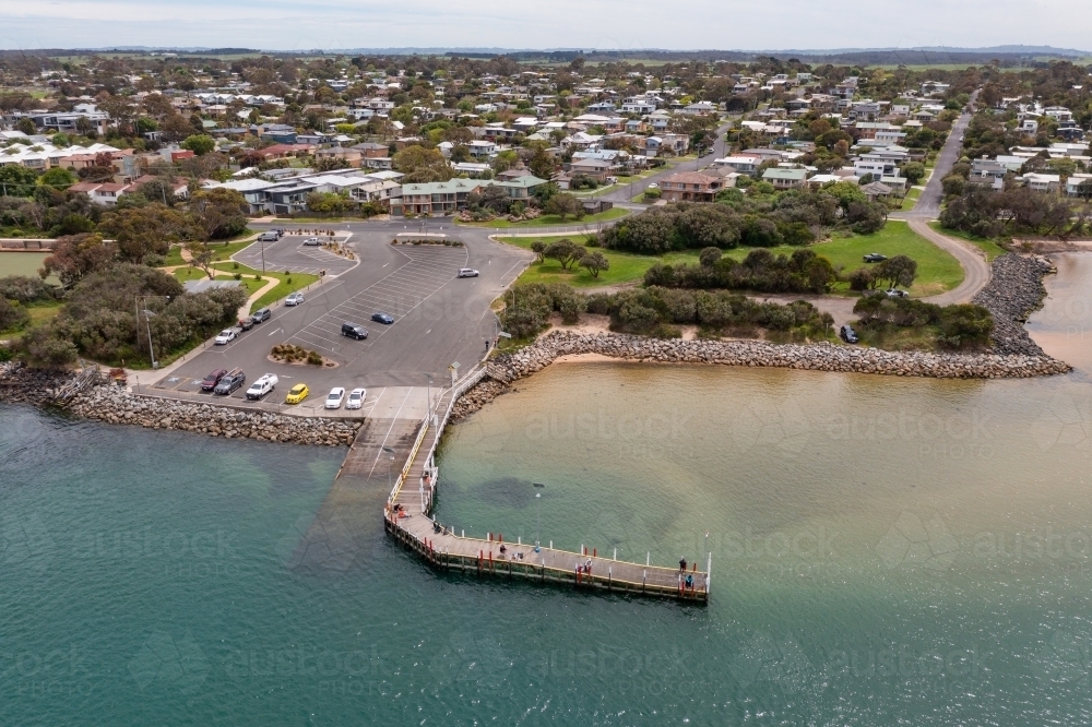 Aerial view of a wooden jetty next to a boat ramp in a coastal town - Australian Stock Image