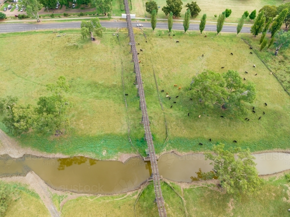 Aerial view of an historic abandoned railway line above green farm land, a creek and a country road - Australian Stock Image