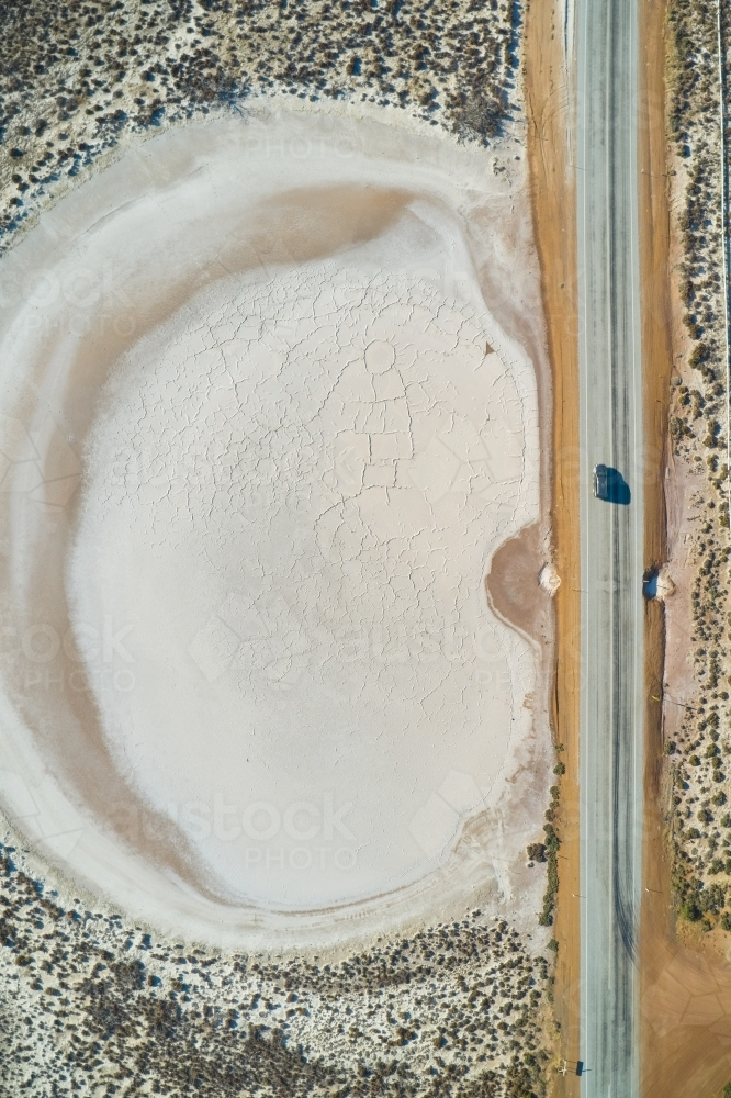 Aerial view of an SUV driving on a bitumen road past a small dry salt lake in rural WA - Australian Stock Image