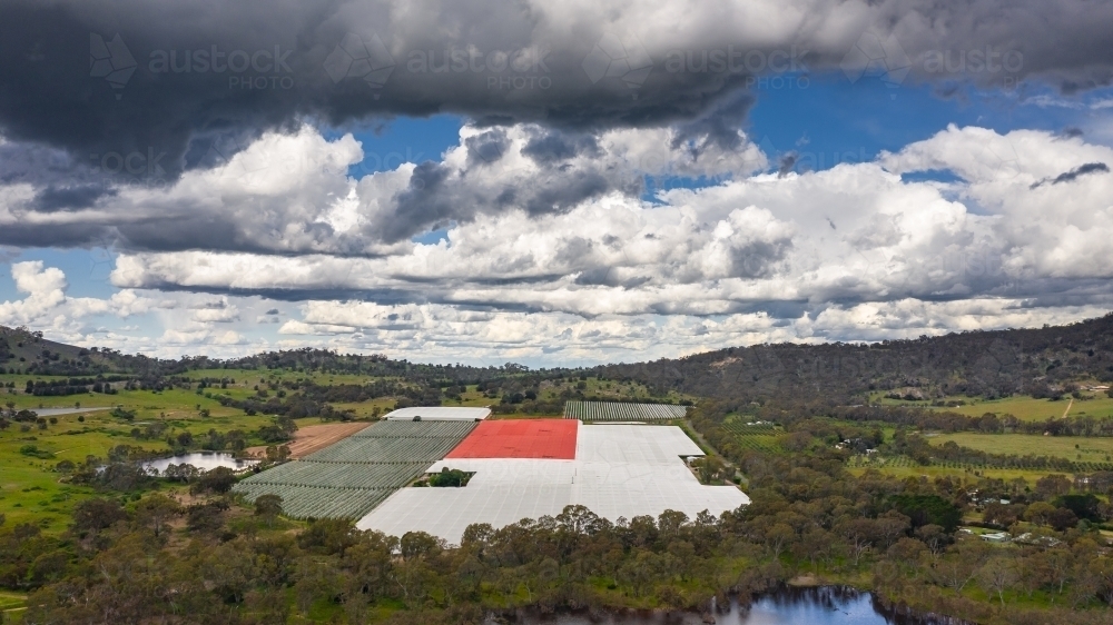 Aerial view of an undercover orchard in a valley under a cloudy sky - Australian Stock Image