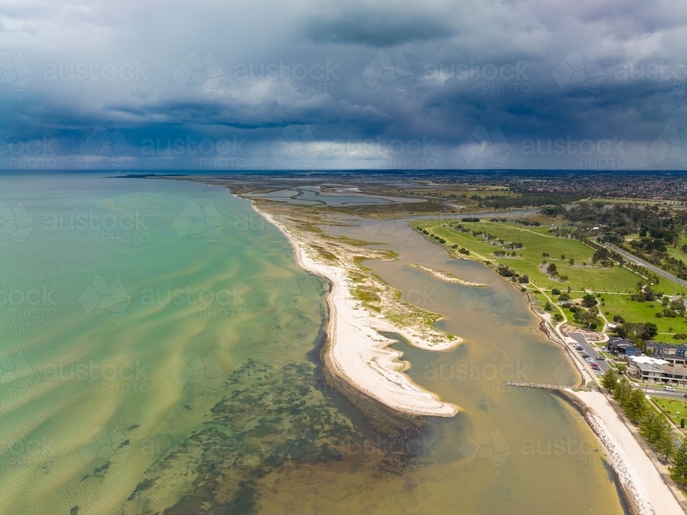 Aerial view of an unusually shaped sand bar running along the coast under dark rain clouds - Australian Stock Image