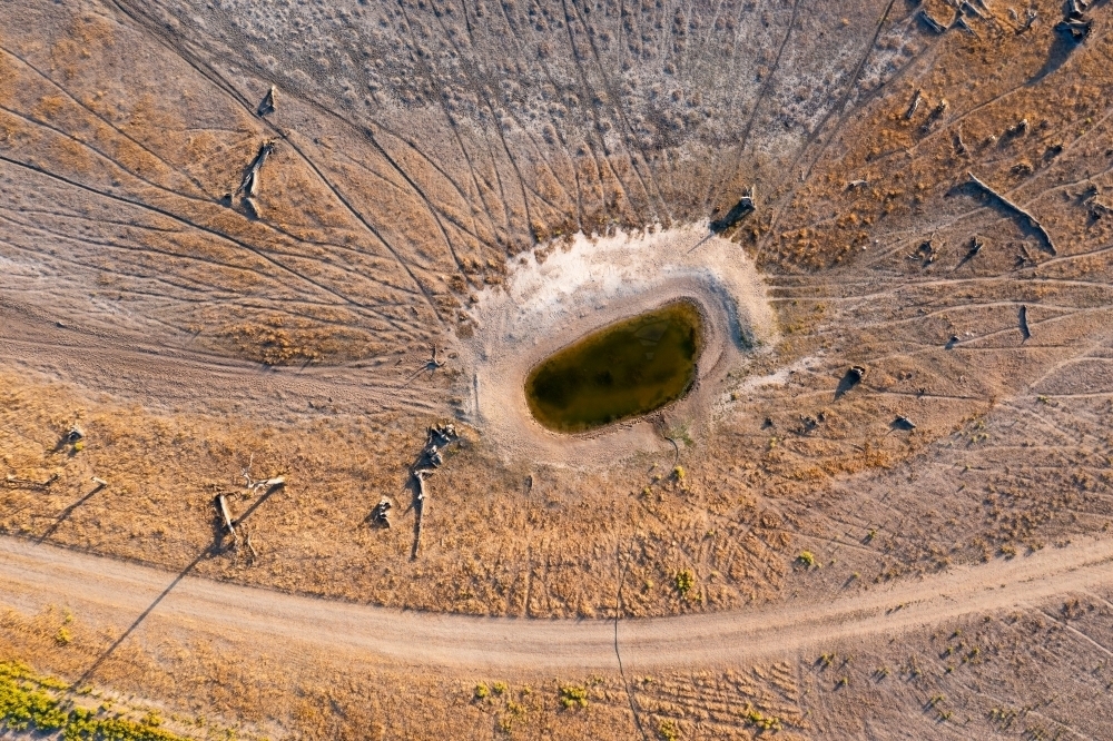 Aerial view of arid farmland with cattle tracks leading to a small waterhole - Australian Stock Image