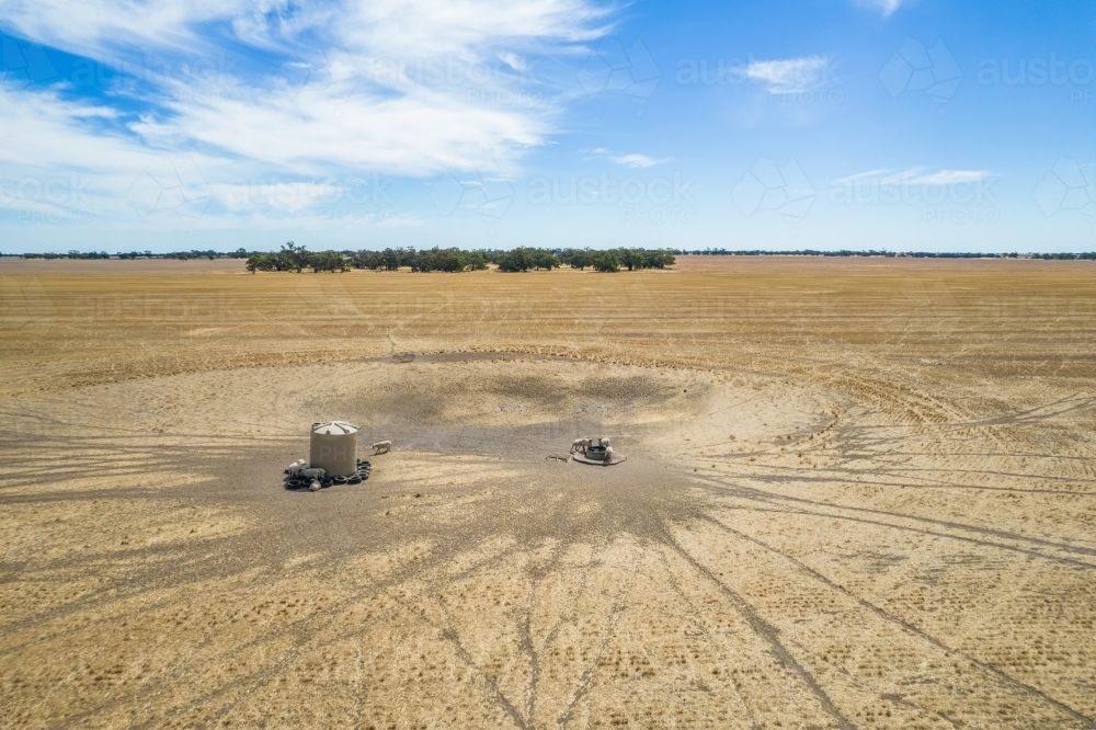 Aerial view of barren landscape with sheep gathering around water tank - Australian Stock Image