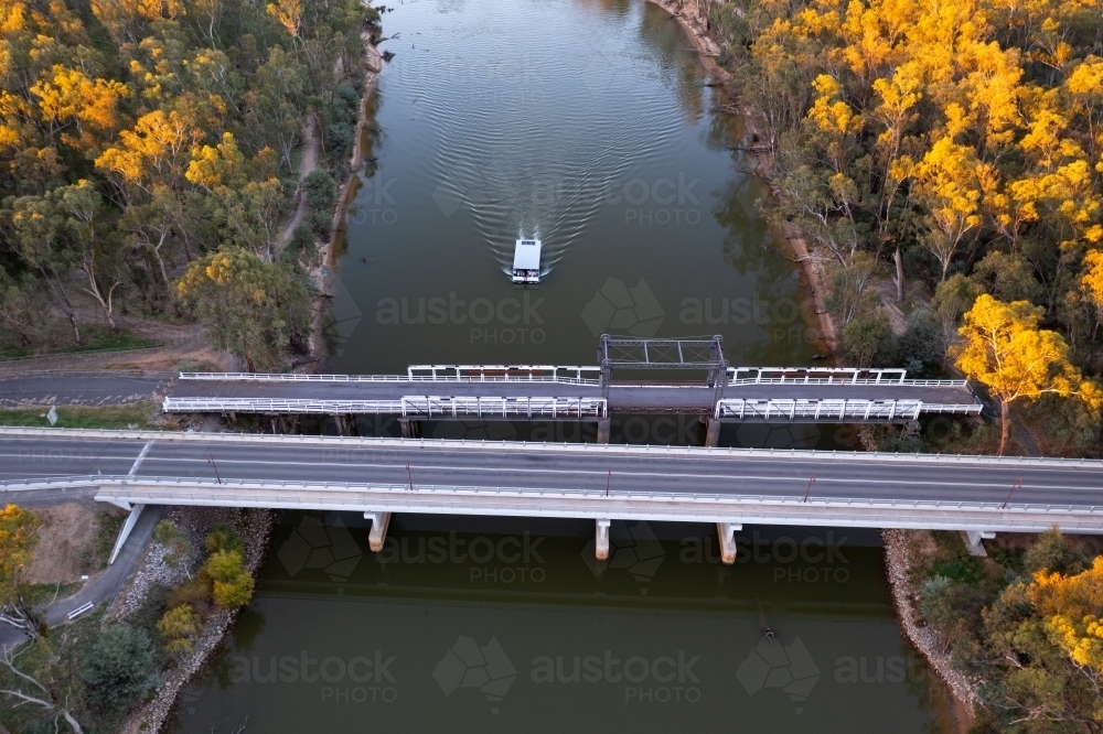 Aerial view of bridges crossing a wide river with a house boast passing underneath - Australian Stock Image