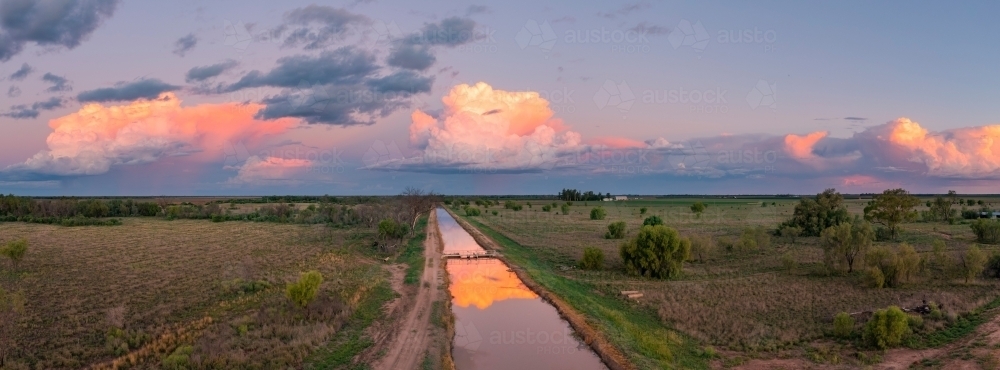 Aerial view of colourful storm clouds at twilight reflected in the water of an irrigation channel - Australian Stock Image