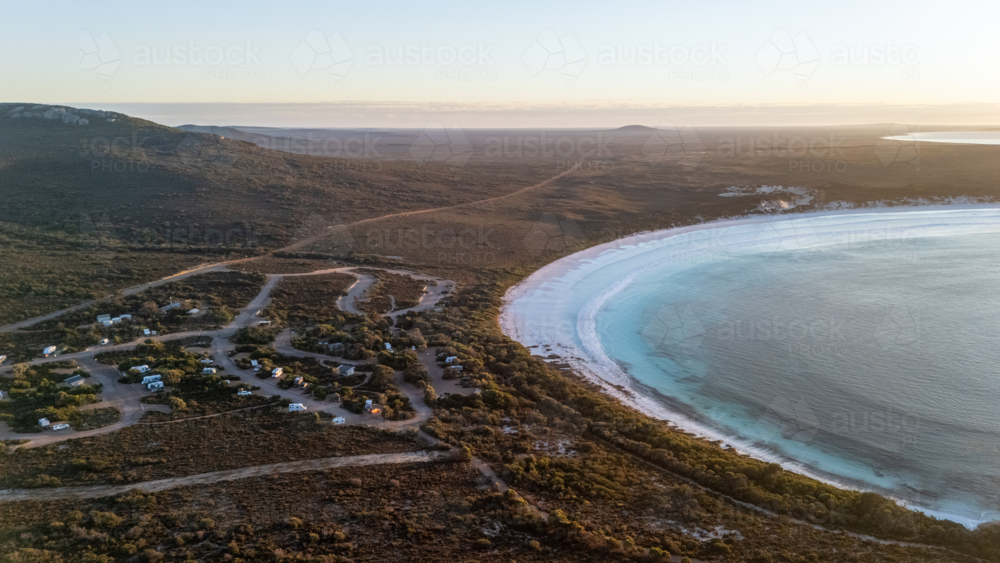 Aerial view of crescent-shaped beach at sunset with caravan park stop - Australian Stock Image