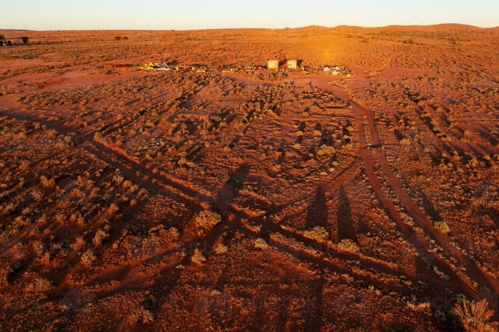 Aerial view of dirt tracks crossing a desert landscape with distant buildings - Australian Stock Image