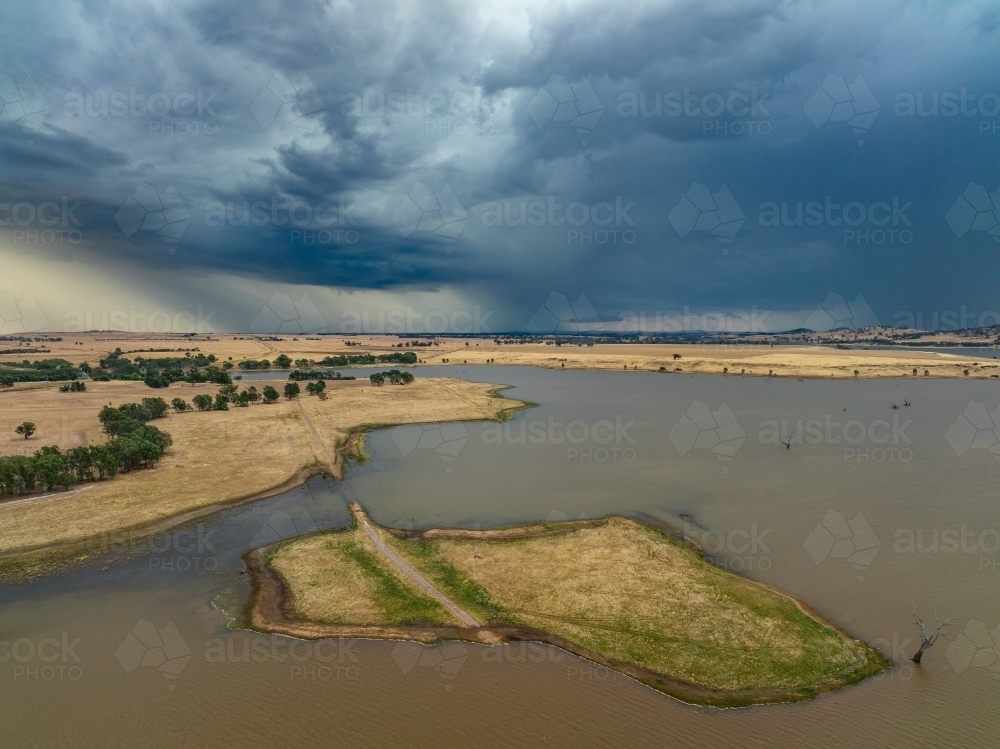 Aerial view of dramatic storm clouds and heavy rain over an island in a murky lake - Australian Stock Image