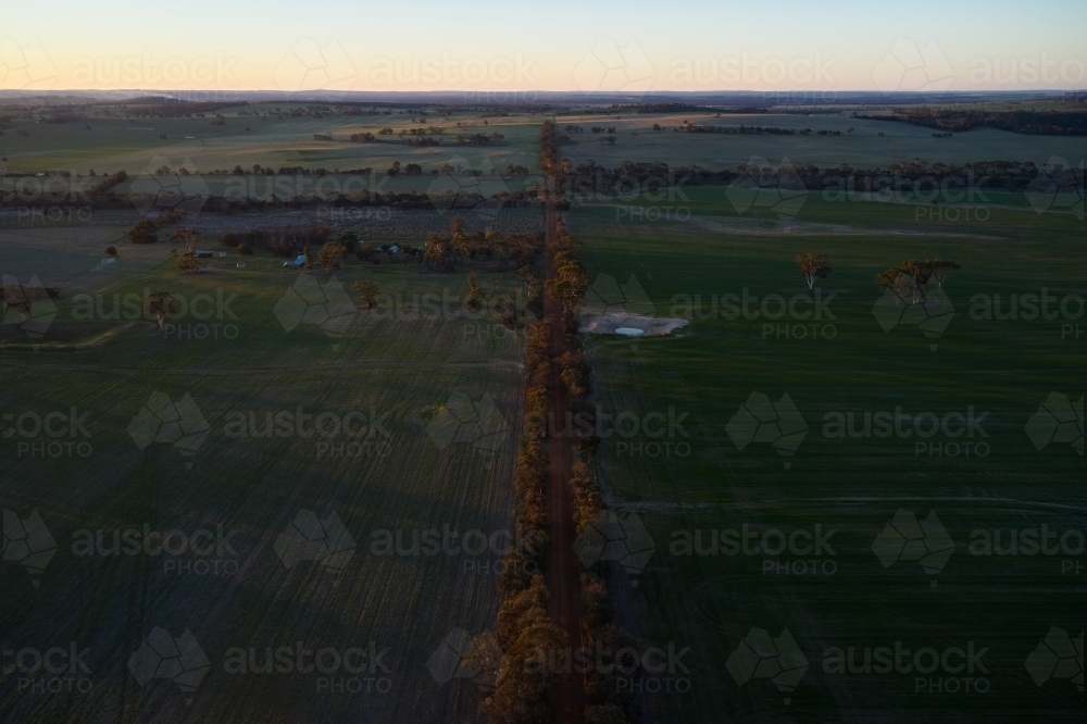 Aerial view of farmland, with cropped fields, a dam and a gravel road in the fading evening light. - Australian Stock Image