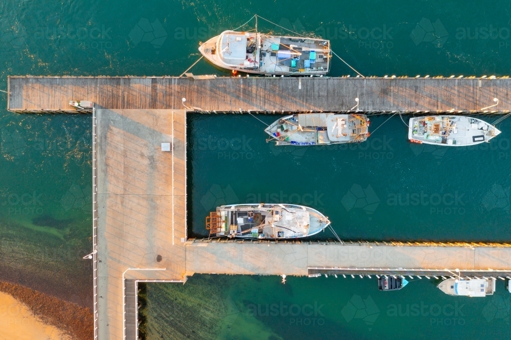 Aerial view of fishing boats docked alongside a jettys over a coastal bay - Australian Stock Image