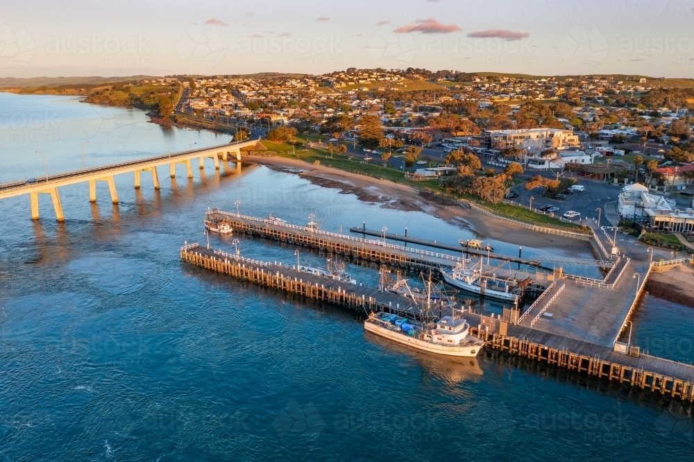 Aerial view of fishing boats docked alongside jetties near a bridge and coastal town - Australian Stock Image