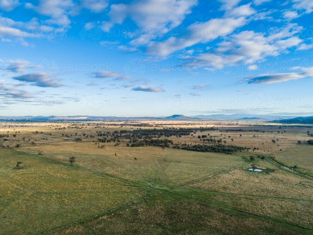 Aerial view of flat Aussie farm paddock with sunlight on grass and hills in distance - Australian Stock Image