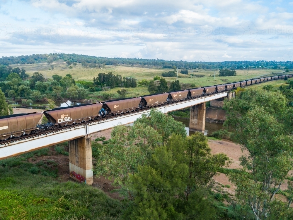 aerial view of full coal train crossing bridge over river - Australian Stock Image