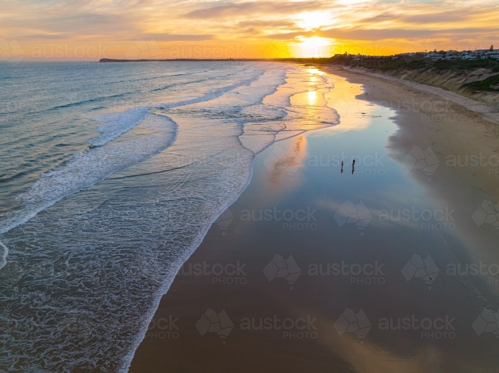 Aerial view of gentle waves on a beach with reflection of a sunset - Australian Stock Image