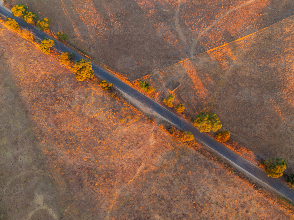 Aerial view of golden evening light on a country road running through dry rural farmland - Australian Stock Image