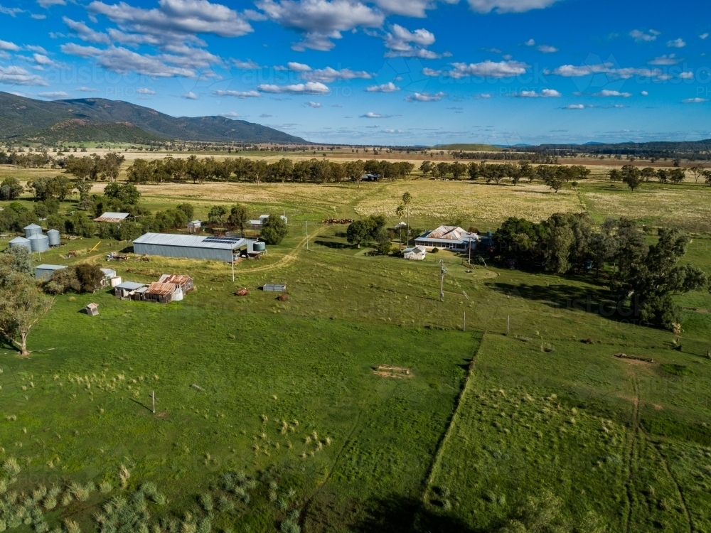 Aerial view of green farm paddock and farm shed beside homestead under bright blue sky - Australian Stock Image