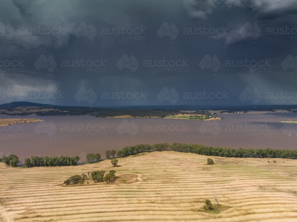 Aerial view of heavy rain falling from storm clouds over a reservoir next to harvested farmland - Australian Stock Image