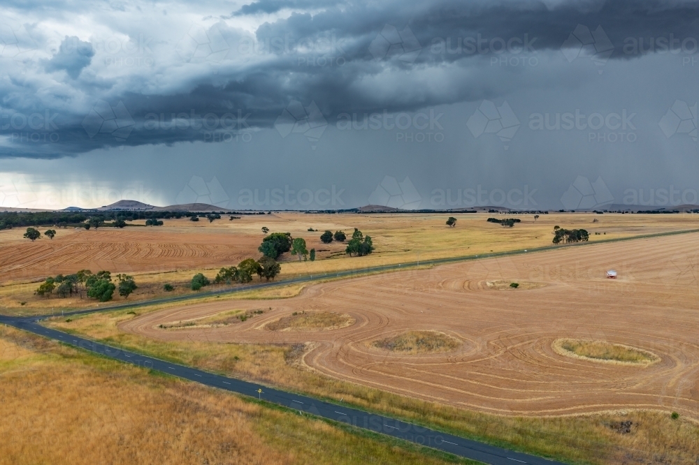 Aerial view of heavy rain falling over country roads and harvested paddocks on rural farmland - Australian Stock Image