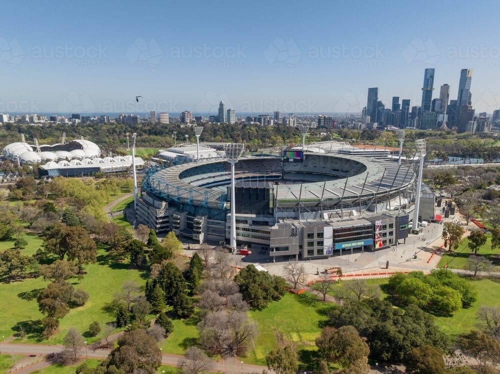 Aerial view of large sporting arena surrounded by parkland with high rise buildings behind - Australian Stock Image