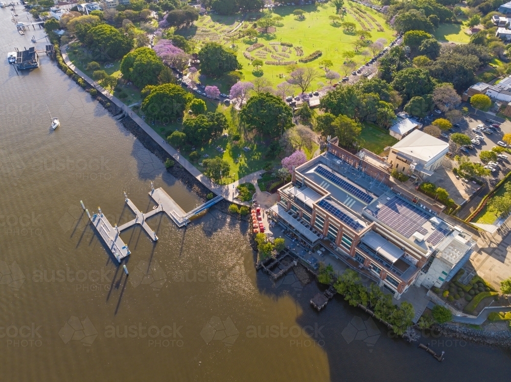 Aerial view of parkland and a large building with a jetty on the banks of a river - Australian Stock Image