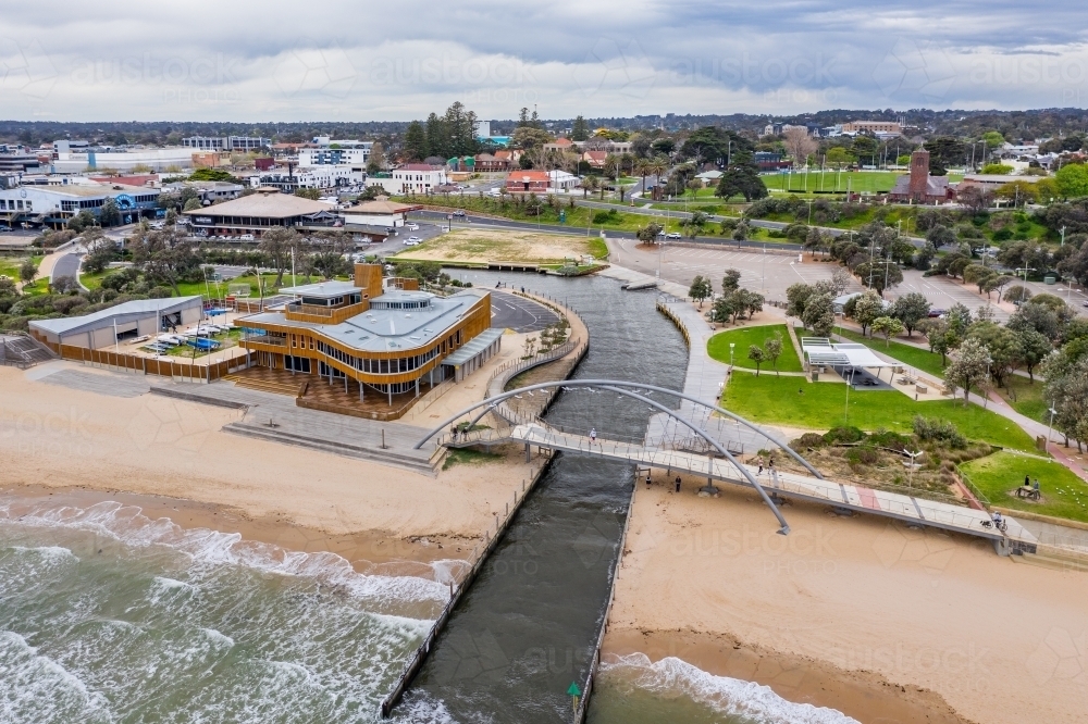 Aerial view of pedestrian bridge over a marina channel cutting through a beach, flowing out to sea - Australian Stock Image