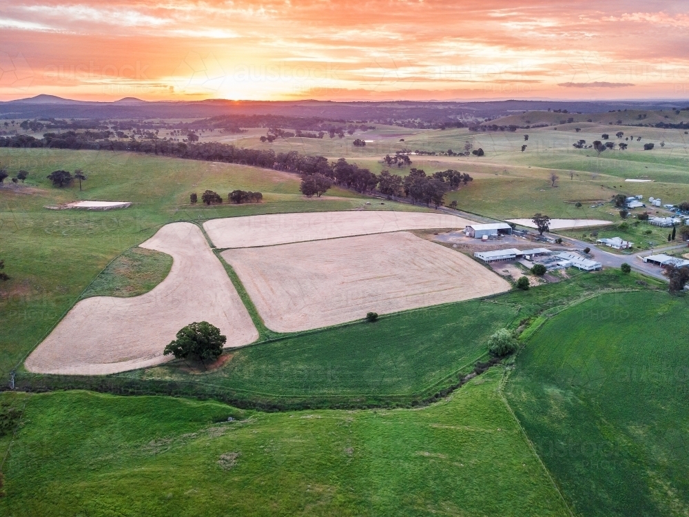 Aerial view of ploughed paddocks near farm buildings at sunset - Australian Stock Image