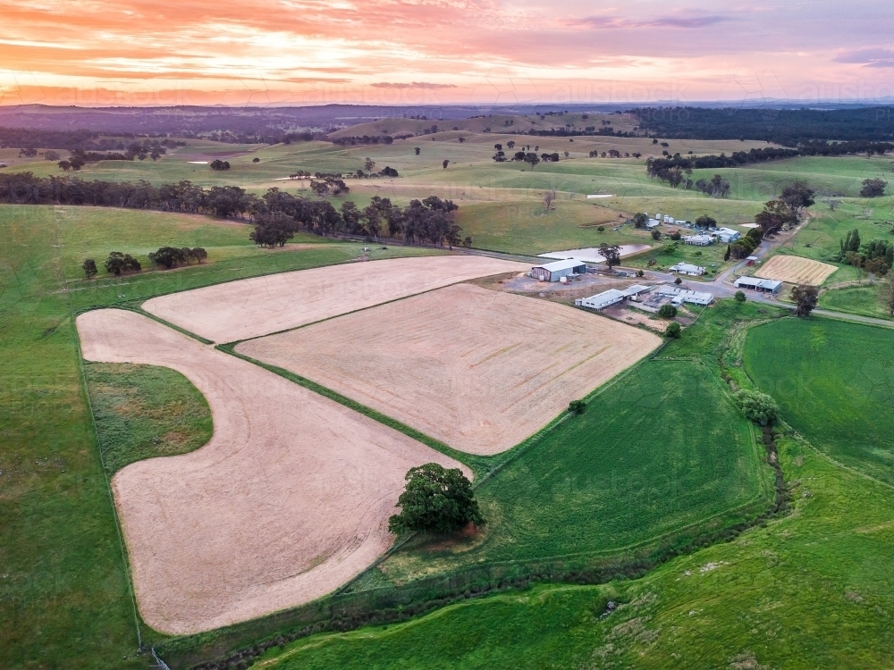 Aerial view of ploughed paddocks near farm buildings at sunset - Australian Stock Image