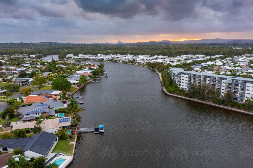 Aerial view of real estate and apartment buildings lining a canal under a dull sunset sky - Australian Stock Image