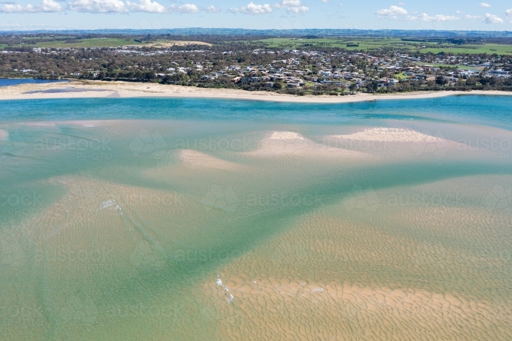 Aerial view of sand bars and patterns in a shallow inlet alongside a coastal town - Australian Stock Image