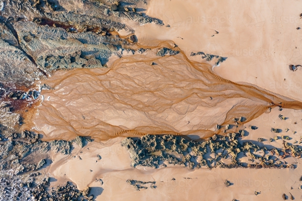 Aerial view of tannin stained creek spreading out over a sandy beach - Australian Stock Image