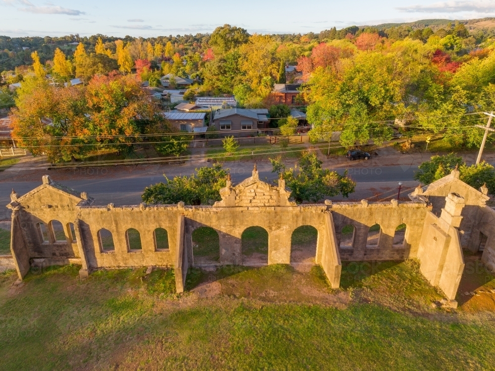 Aerial view of the remains of an historic building facade with arches surrounded by Autumn trees - Australian Stock Image